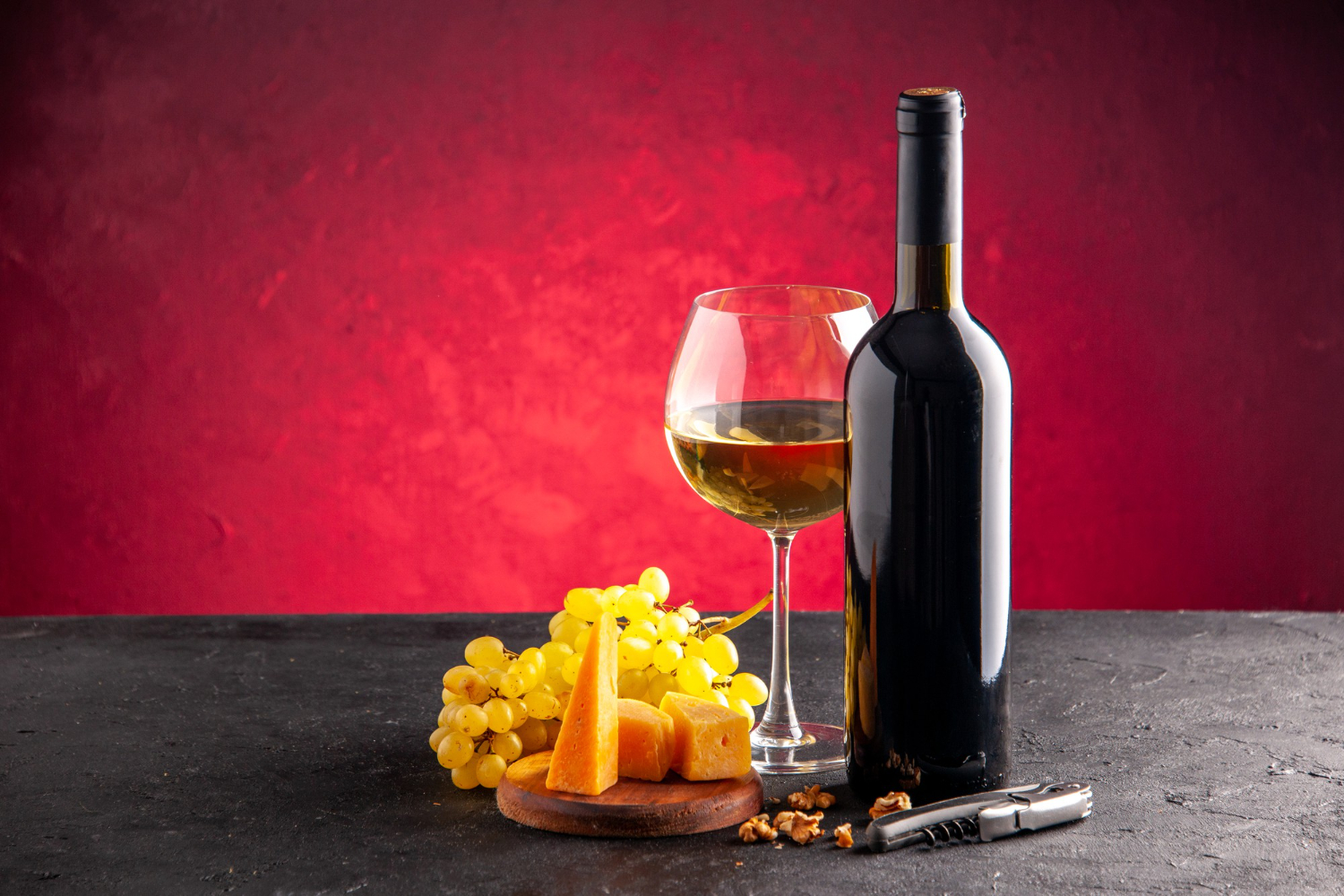 front-view-wine-glass-wine-bottle-yellow-grapes-cheese-wood-board-wine-opener-dark-table-light-red-background.jpg