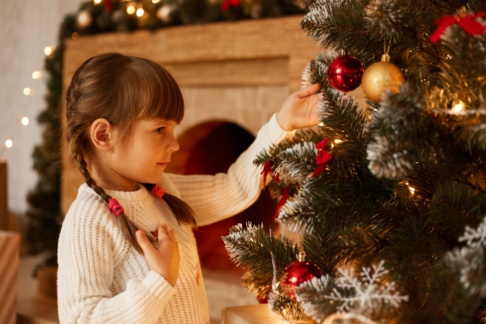 side-view-portrait-charming-little-girl-with-pigtails-decorating-christmas-tree-alone-wearing-white-sweater-standing-living-room-near-fireplace.jpg