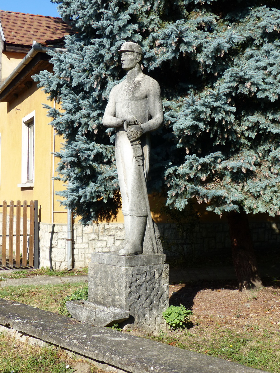 Az emlékmű mellett álló, szocreál stílusú bányász szobor