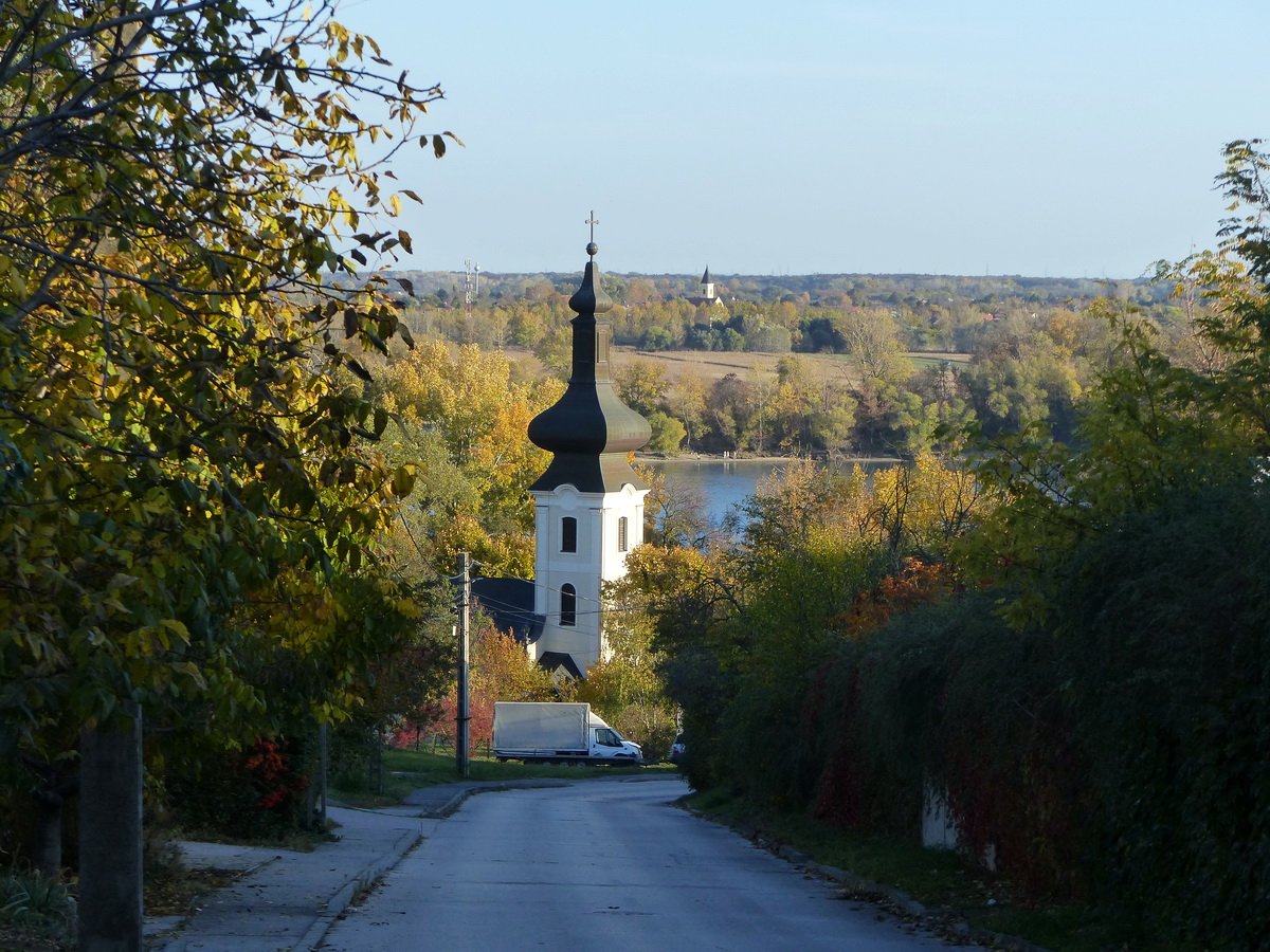 Ereszkedés a Hét vezér utcán a százhalombattai ófaluba. Előtérben a százhalombattai görögkeleti templom, háttérben a Csepel szigeten Tököl templomtornya áll.