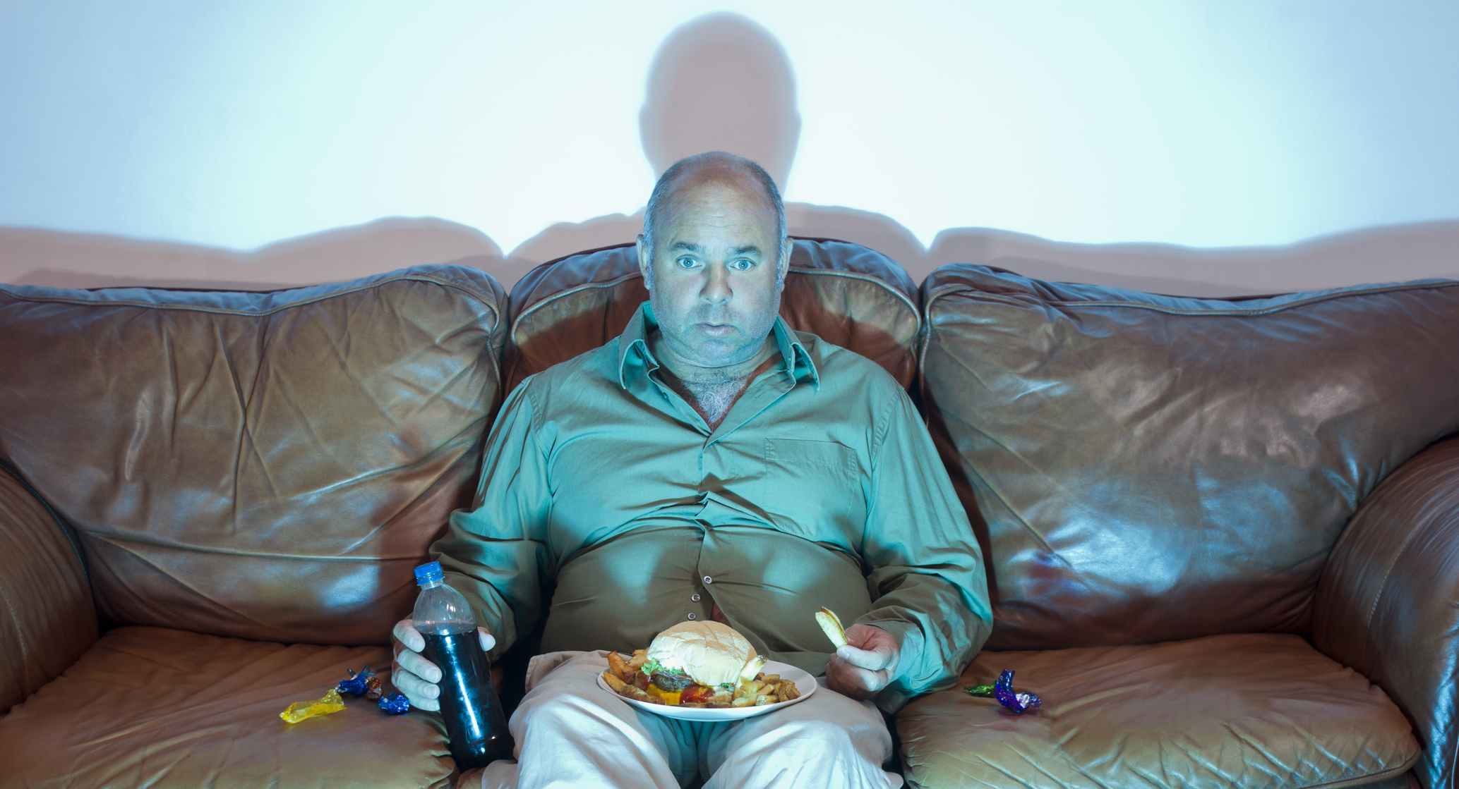 a-mature-overweight-man-sitting-on-an-old-couch-watching-tv-with-an-unhealthy-meal-of-hamburger-french-fries-and-soda-pop-2.jpg