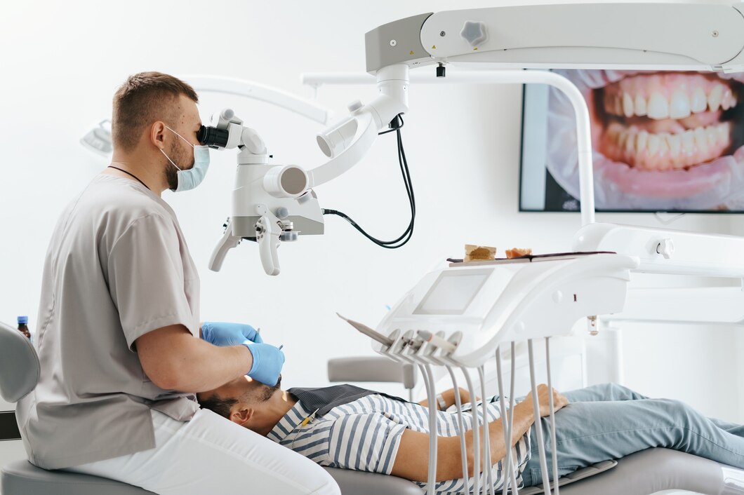 young-man-with-patient-bib-dental-chair-dentist-who-sits-him-he-looks-his-teeth-using-dental-microscope-holds-dental-bur-mirror_158595-7731.jpg