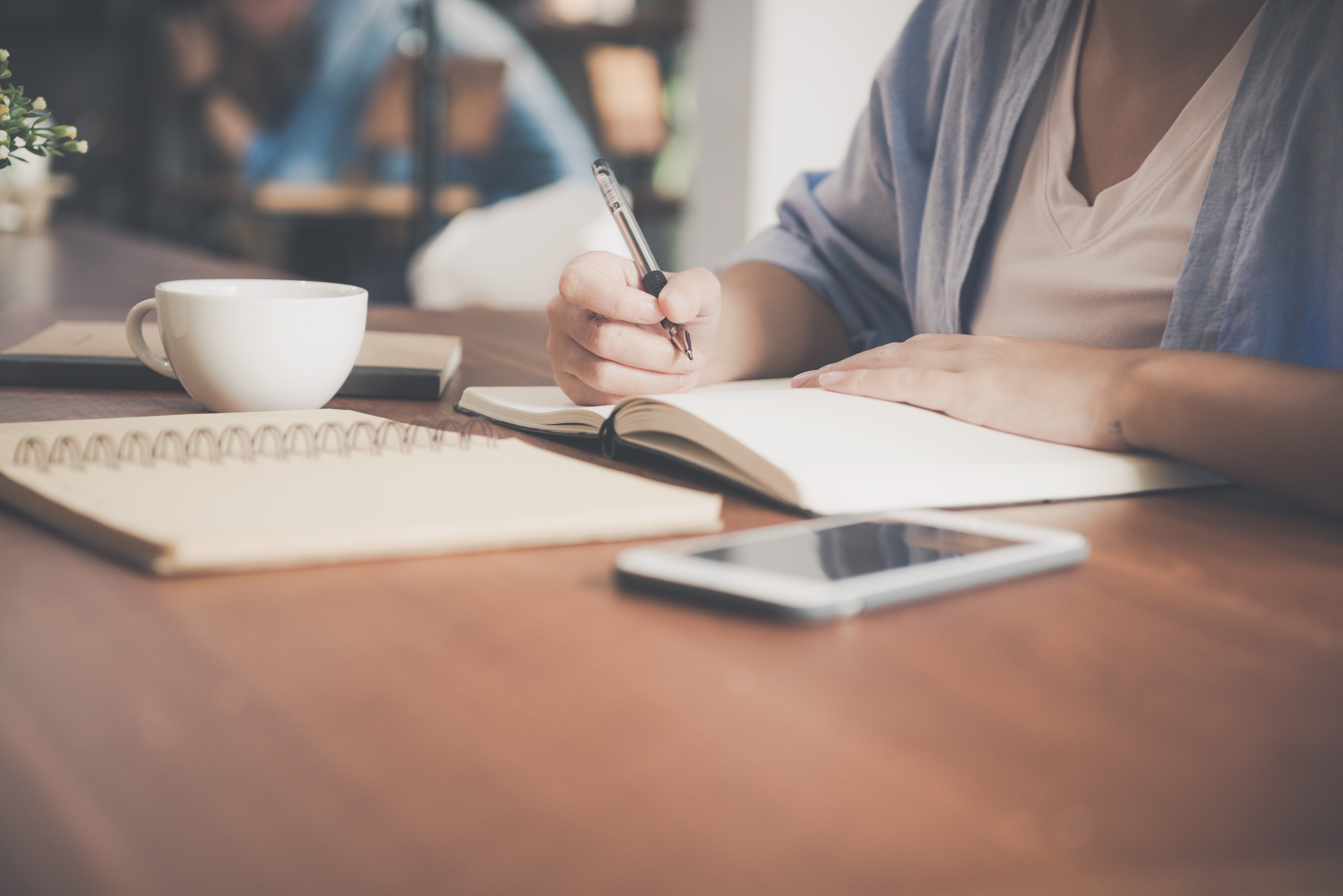 woman-writing-on-a-notebook-beside-teacup-and-tablet-733856.jpg