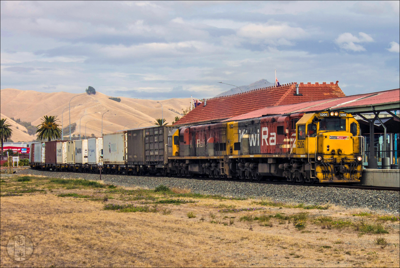 KiwiRail DXC (GE U26C) halad át tehervonatával a blenheimi állomáson. A Picton – Christchurch vonal mentén fekvő Blenheim egyébként saját konténerterminállal is rendelkezik a várostól északra fekvő Spring Creek határában, melyet egy pár tehervonat szolgál ki Pictonból a hét öt napján.