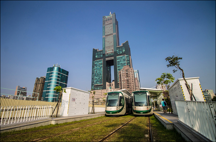 A KMRT villamosai Kaohsiung Exhibition Center (高雄展覽館, gāoxióng zhǎnlǎnguǎn) megállóban, háttérben a 347,5 méter magas 85 Sky Tower.