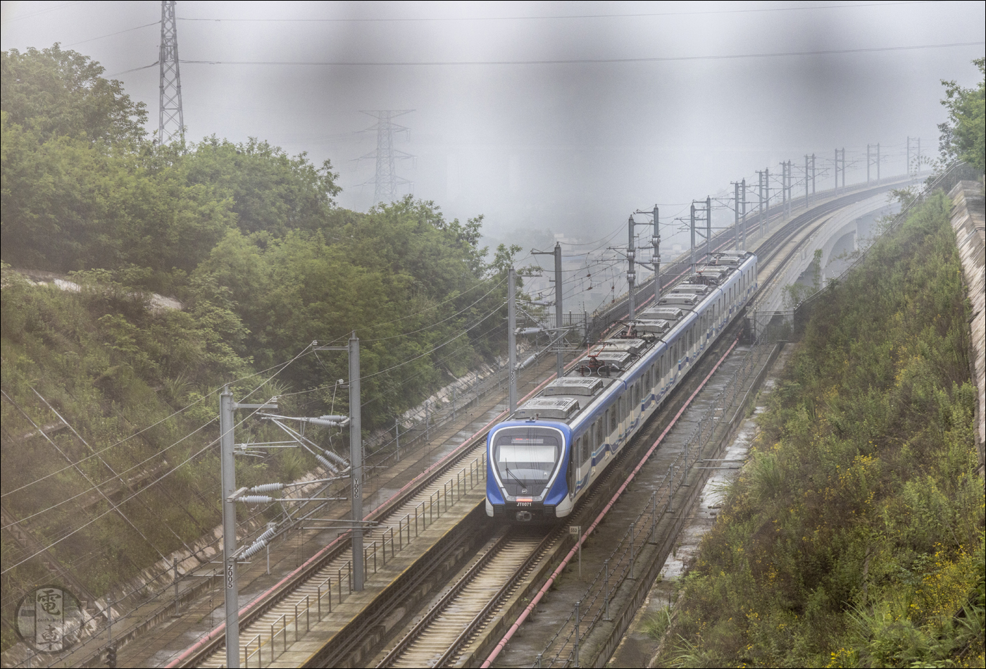 Ezen a végtelenül igénytelen képen a Jiangtiao vonal egyik, CRRC CCD5051-es típusú motorvonatát láthatjuk Jiulongyuan állomás közelében útban Tiaodeng felé. Itt nem a fényképezőgép szenzora mondta fel a szolgálatot, csak egy rendkívül apró lyukú kerítésen át voltam kénytelen fotózni, mivel nem akartam kerülni a bevágás végei felé, illetve letaposni Wang bácsi káposztását, kockáztatva, hogy rámhívja a rendőrőket, mondván, hogy egy külföldi idióta épp szétdíbolja a veteményest.