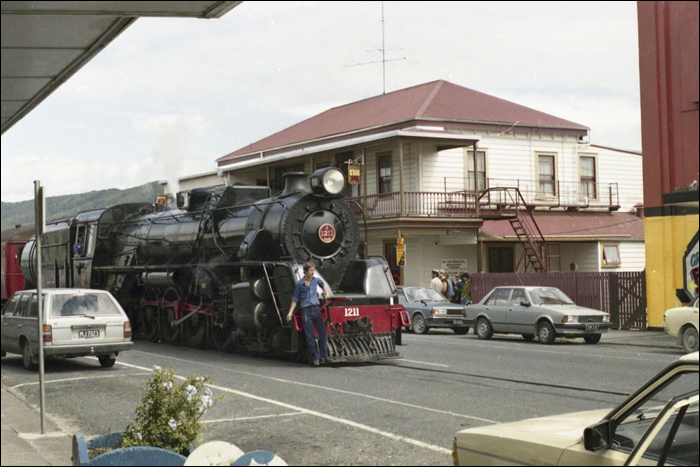 Az egykori NZR egy J sorozatú gőzmozdonya szeli át Kawakawa belvárosát 1984-ben, egy évvel a Kawakawa – Opua szakasz bezárása előtt. (Fotó: Les Downey)