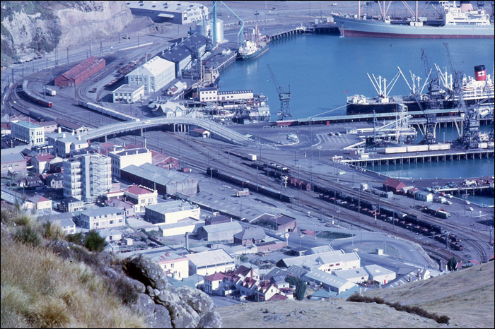 A lytteltoni kikötő 1969-ben. E képhez rengeteg közlekedéstörténelmi eseményt lehet kapcsolni, hiszen egy évvel korábban, 1968. április 10-én süllyedt el a  Wellington – Lyttelton viszonylaton közlekedő TEV Wahine Wellington közelében. A járművet üzemeltető  Union Steam Ship Co. végül 1976-ban, több mint 80 év után, e baleset és az akkoriban már jelentősnek mondható légiközlekedés hatására szüntette meg véglegesen a tengeri összeköttetést a két város között. Bár vasúti járműveket szállító kompok itt sosem közlekedtek, 1902-től a személyvonatok a képen is megfigyelhető kiágazás segítségével gyakorlatilag a kompok mellett állhattak meg, megspórolva az utasoknak a csomagokkal való kóválygást. (Fotó: Anthony McIlwain)