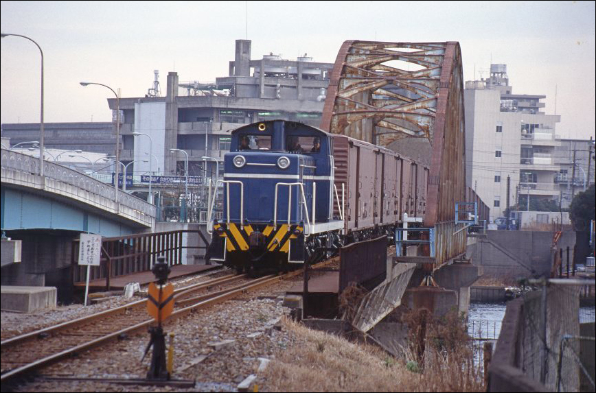 A tokiói kikötőnek egykor Tokió Kikötői Vontatási Igazgatóság néven saját vasúttársasága volt. A képen e társaság egyik D60-as sorozatú járművét láthatjuk néhány fedett teherkocsi társaságában a ma is álló Harumi-hídon. A JNR DD13-as sorozatú mozdonyokkal teljesen megegyező járművekből összesen 3 került a tokiói kikötőbe 1956 és 1967 között, napjainkra azonban sajnos egy sem maradt fenn, hiszen 2005-ig valamennyi ilyen mozdonyt selejtezték. (Forrás: Twitter)