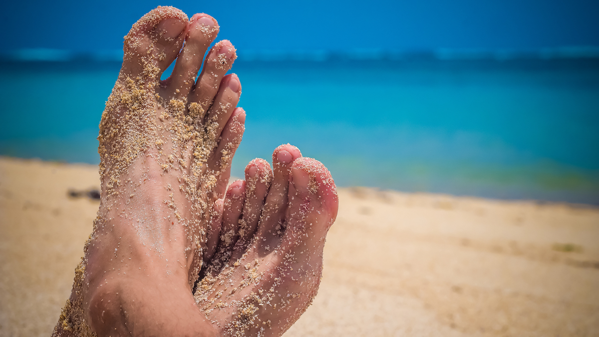 male-cross-feet-at-the-sandy-beach-ocean-in-backgr-w5j23zj.jpg