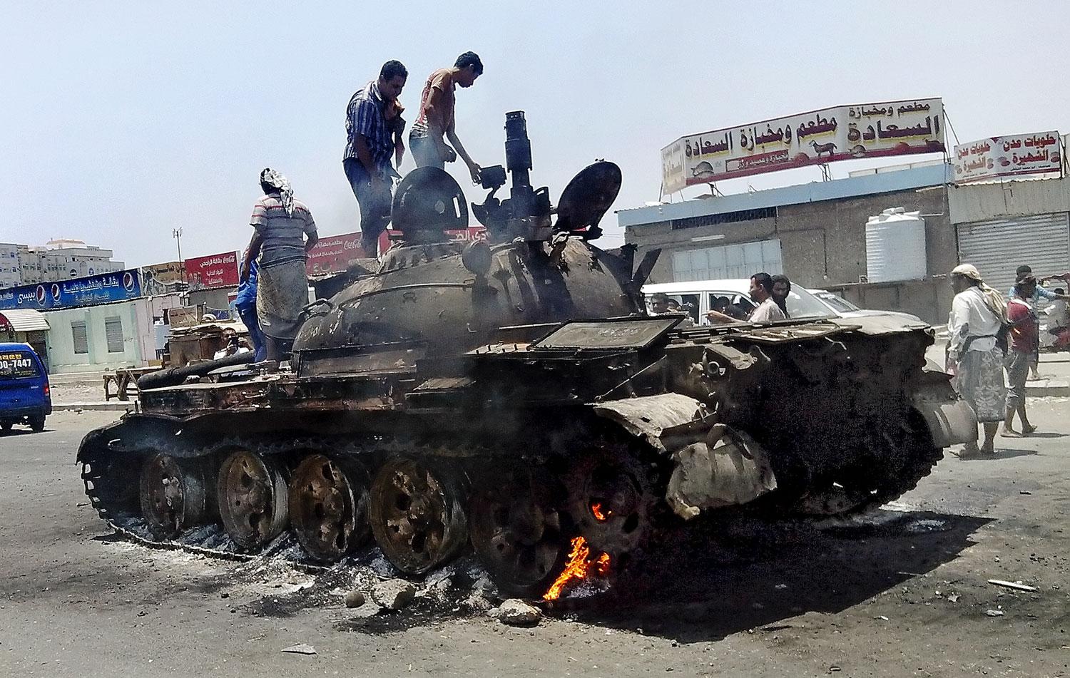 Helyi lakosok szemrevételezik a kiégett tankot a jemeni Ádenben. A húszi síita felkelők ellen több környező arab állam is fellépett, az országban teljes a káosz. (f.: Reuters)