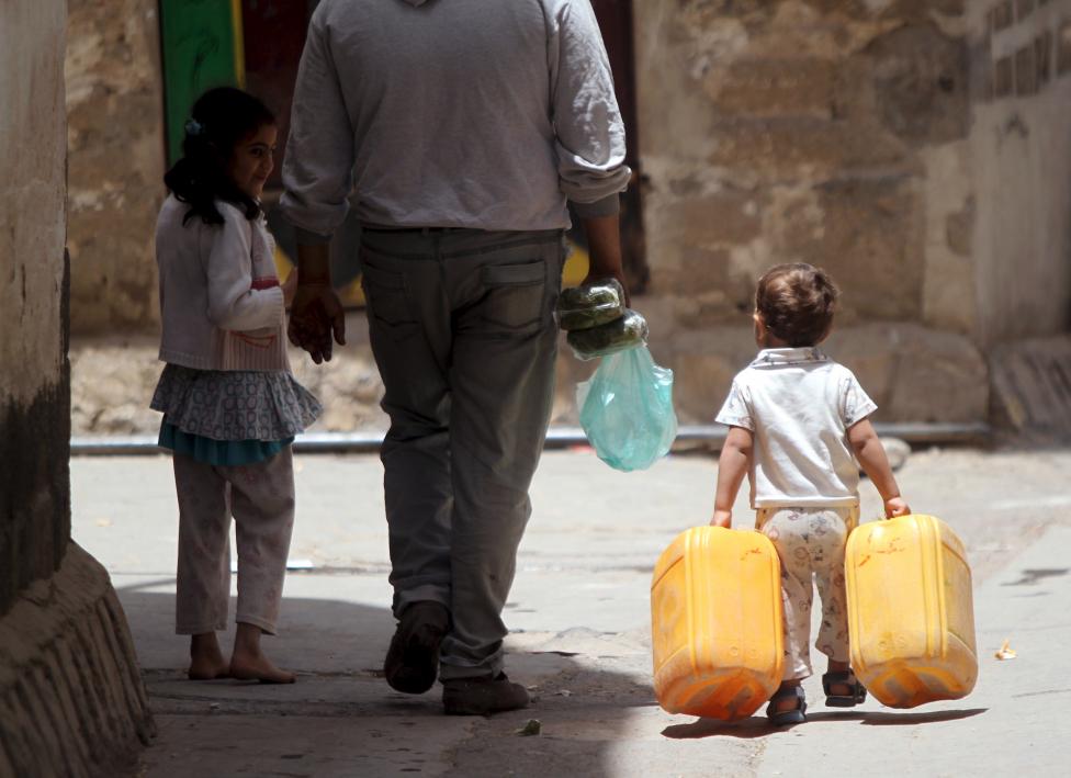 Egy kisfiú cipel vizes ballonokat apjával és nővérével a jemeni Sanaa utcáin. (f.: Reuters)