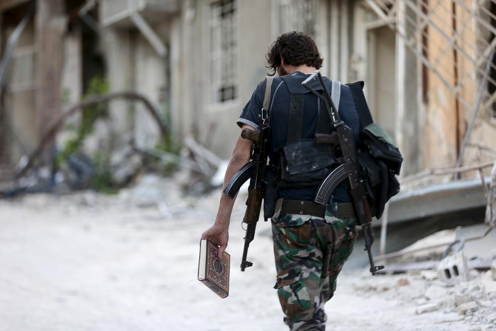 Szíriai felkelő fegyveres sétál a romos utcán, kezében a Koránnal. (f.: Reuters)