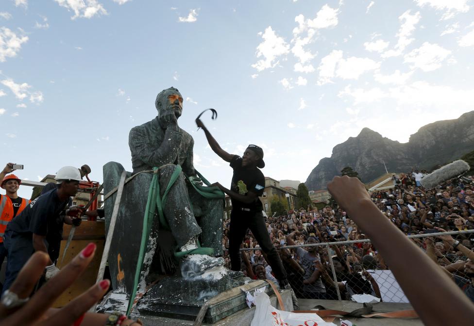Egy egyetemi hallgató ütlegeli övével Cecil John Rhodes éppen eltávolítás alatt álló szobrát a Dél-Afrikai Köztársaság Cape Town-i Egyetemén. Rhodes a brit imperializmus és gyarmatosítás nagy alakja volt, szobrának eltávolítása szimbolikus értékkel bír az elnyomó apartheid rendszer 2 évtizedes bukása után.