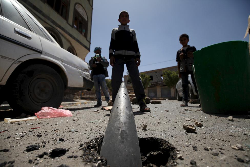 Gyerekek állnak szemben egy az aszfaltba fúródott, fel nem robbant tüzérségi gránát előtt a jemeni Sanaa-ban. (f.: Reuters)