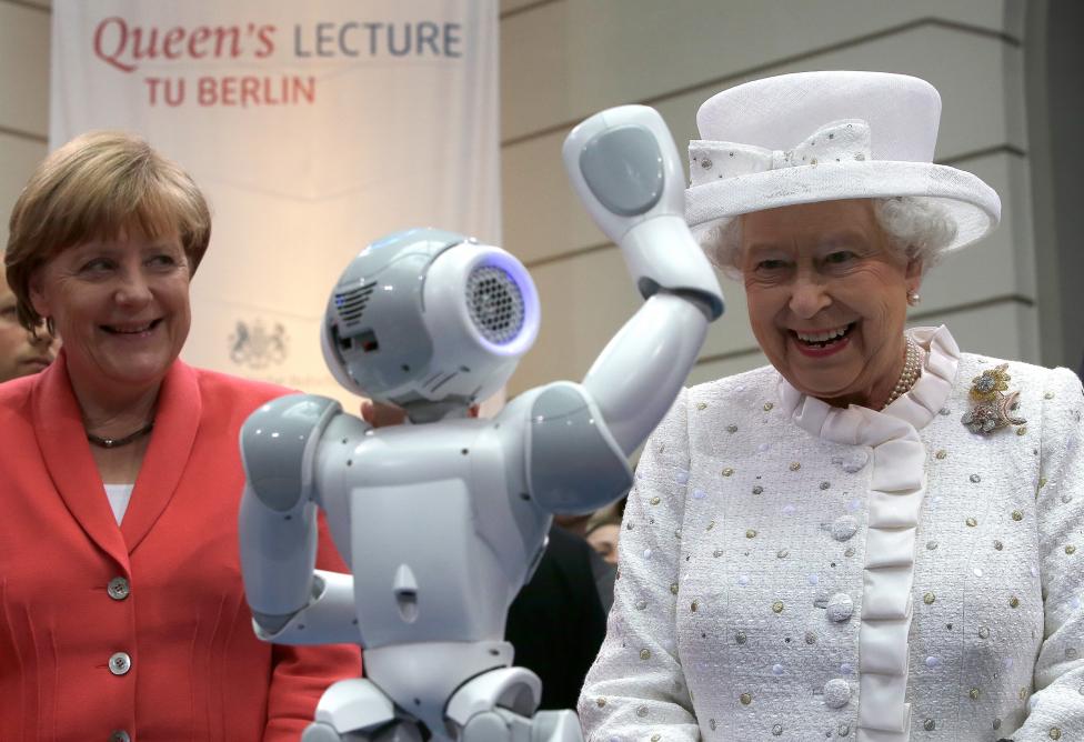 Angela Merkel német kancellár és II. Erzsébet brit királynő mosolyog, miközben egy robot integet nekik. A királynő három napot töltött Németországban, itt épp a Berlini Műszaki Egyetemet látogatták meg együtt. (f.: Reuters)