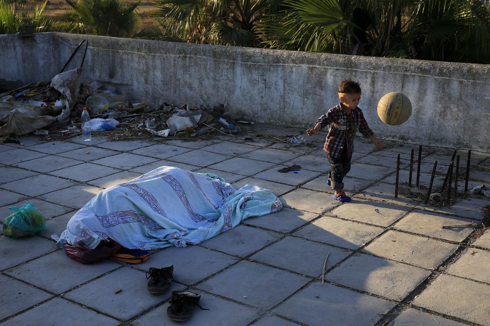 Bevándorló pakisztáni kisgyerek labdázik alvó apja mellett egy elhagyatott hotel tetején, a görög Kos szigeten. A megnövekedett migrációs hullám miatt a görög hatóságok egy stadionba zárták 24 órára a bevándorlók egy részét, többen pedig elhagyatott épületekben, hotelekben szállásolták el magukat. (f.: Reuters)