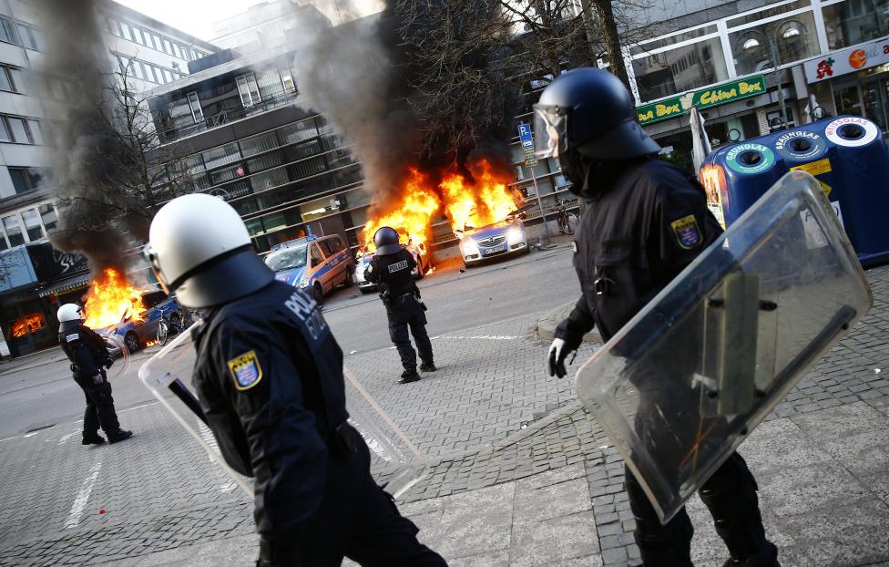 Égő rendőrautók a rohamrendőrök hátterében. A tüntetők legfőképp az Európai Unió megszorításos gazdaságpolitikai intézkedései ellen próbáltak felszólalni. A kezdetben békés felvonulás több helyen eldurvult. (f.: Reuters)