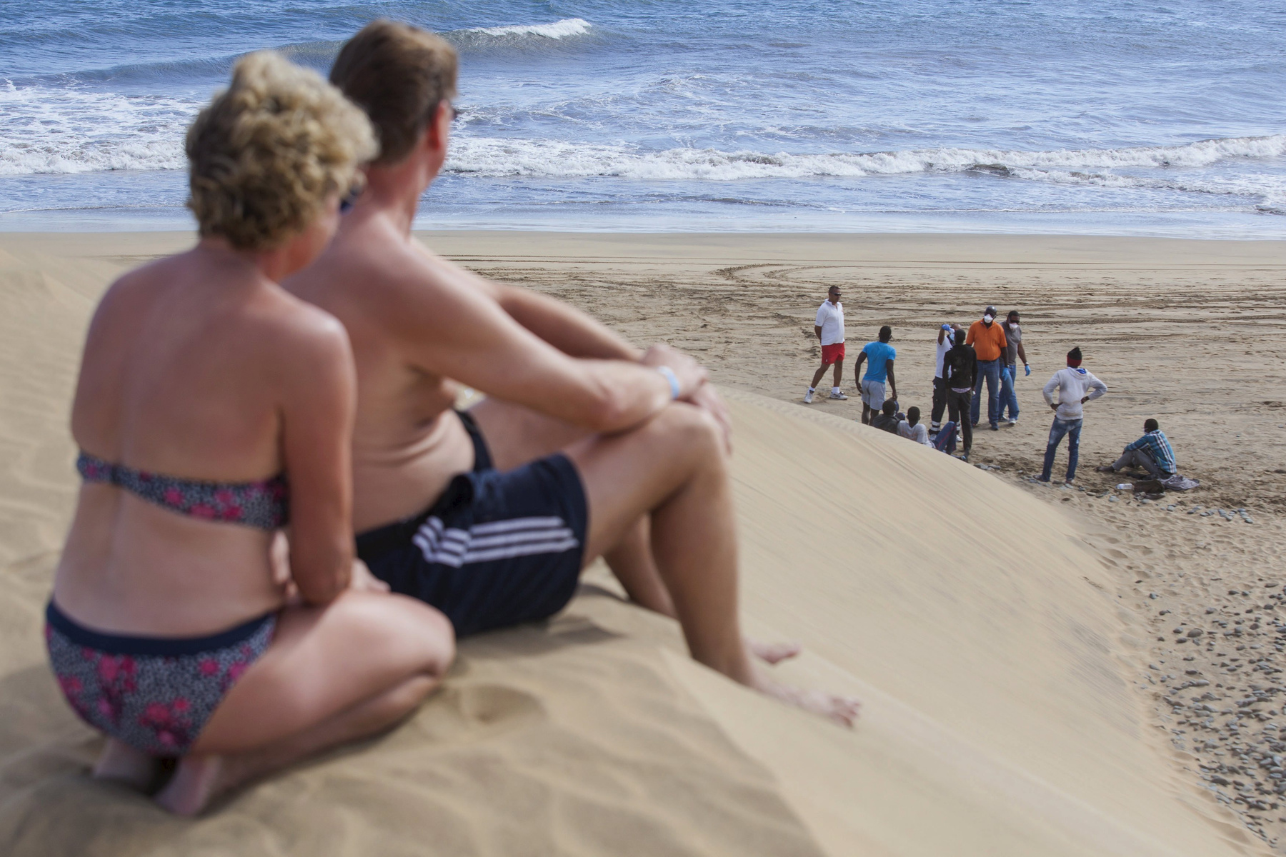 Napozó turisták figyelik a partra érkező menekülteket a Kanári-szigeteken. (f.: AFP)