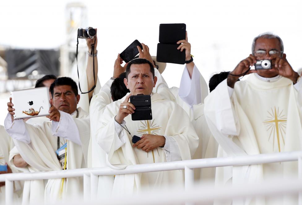 A kórusban álló papok készítenek fényképet a misére érkező Ferenc pápáról Ecuadorban. (f.: Reuters)