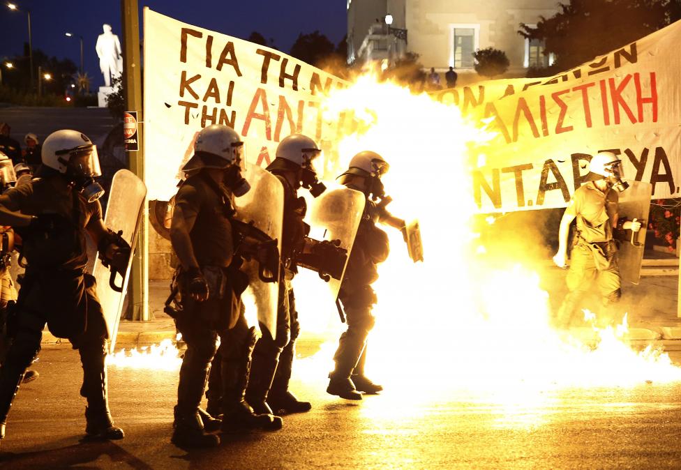 Rohamrendőrök állnak egy épp berobbanó benzines bomba előtt, miközben tömegek tüntetnek az athéni parlament előtt. A görög társadalom nehezen fogadja el, hogy hiába volt népszavazás a megszorítások elutasításáról, a kormány nagyon kemény feltételeket vállalt a gazdasági válságból való kilábalás érdekében. (f.: Reuters)