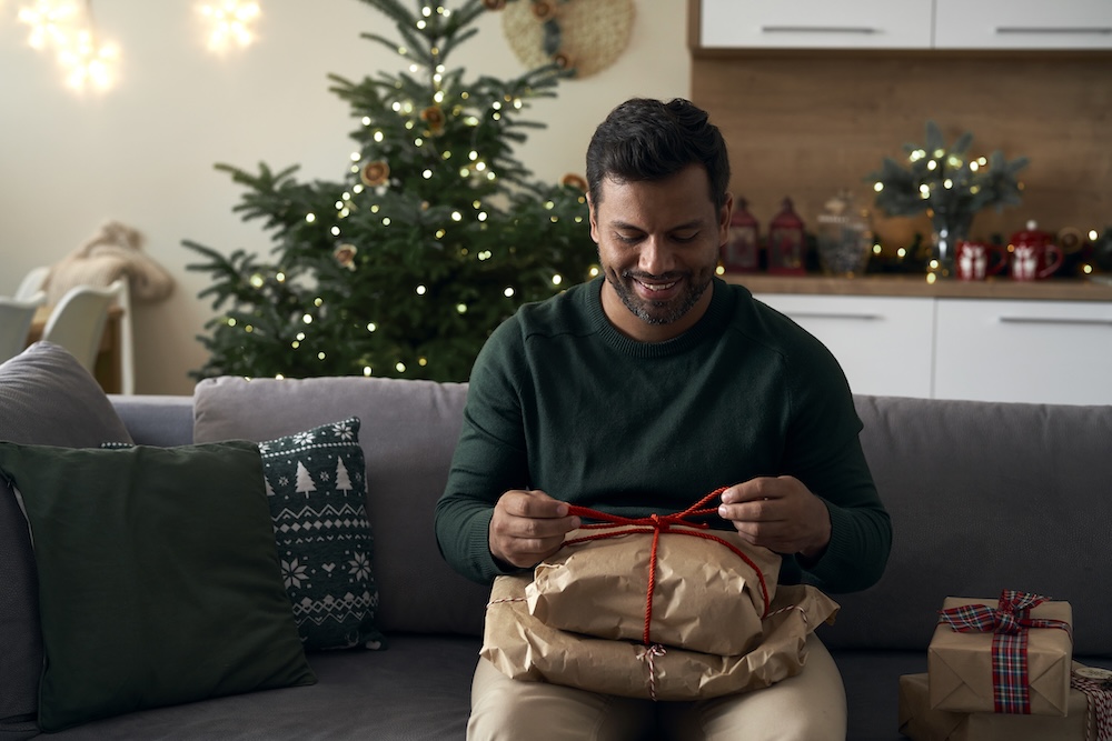 latino-man-with-christmas-present-sitting-on-sofa-2023-11-27-05-22-13-utc.jpg