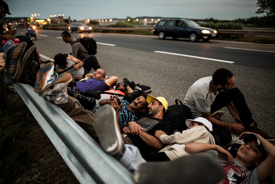 Bielik István: Budapestről az osztrák határ felé gyalogoló szíriai menekültek pihennek az M1-es autópálya mellett, Magyarország, 2015. (c) Bielik István