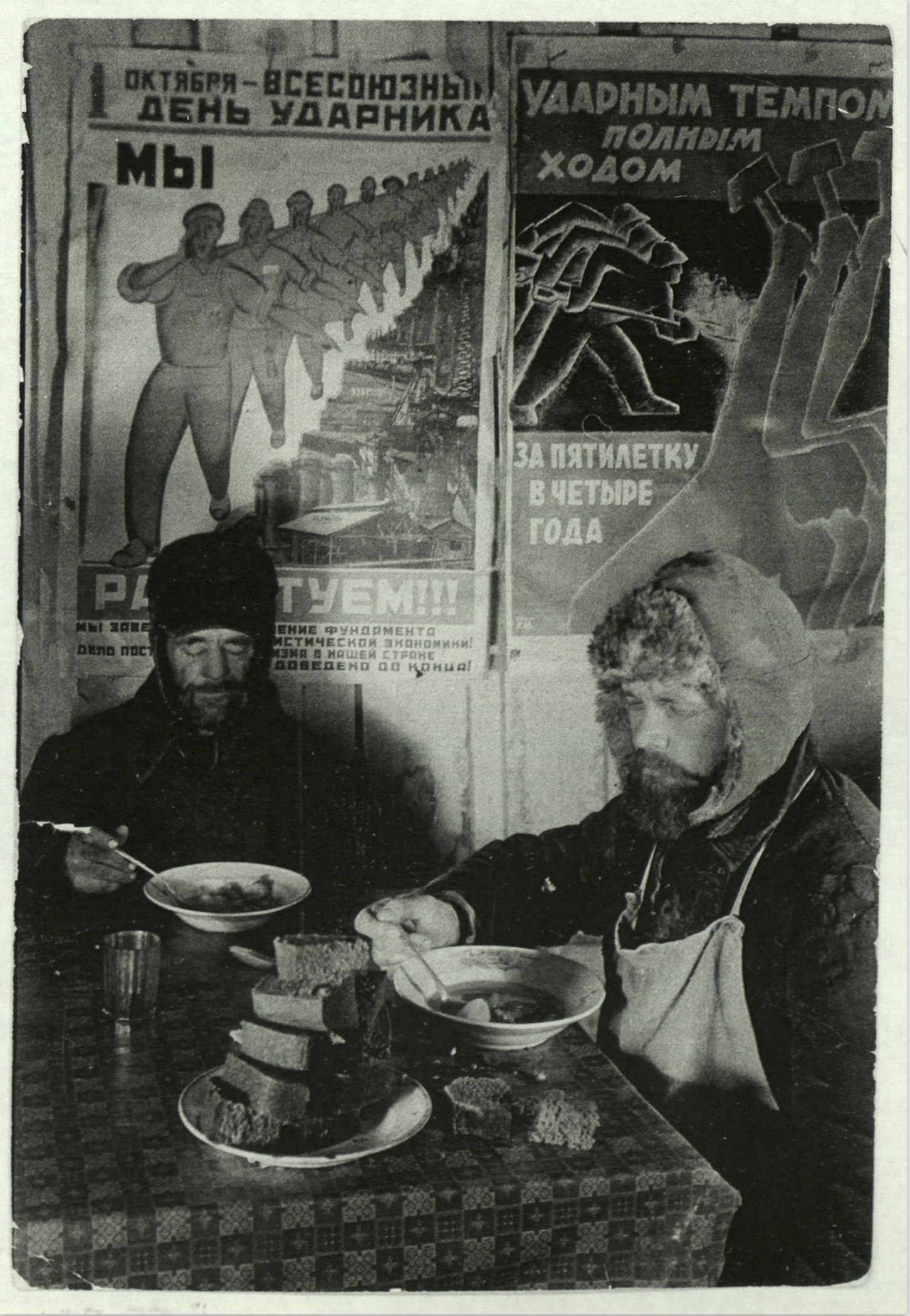 margaret-bourke-white-two-russian-workers-eating-black-bread-and-soup-at-a-table-in-front-of-a-wall-covered-with-soviet-communist-workers-posters-in-siberia-magnitogorsk-1931.jpeg