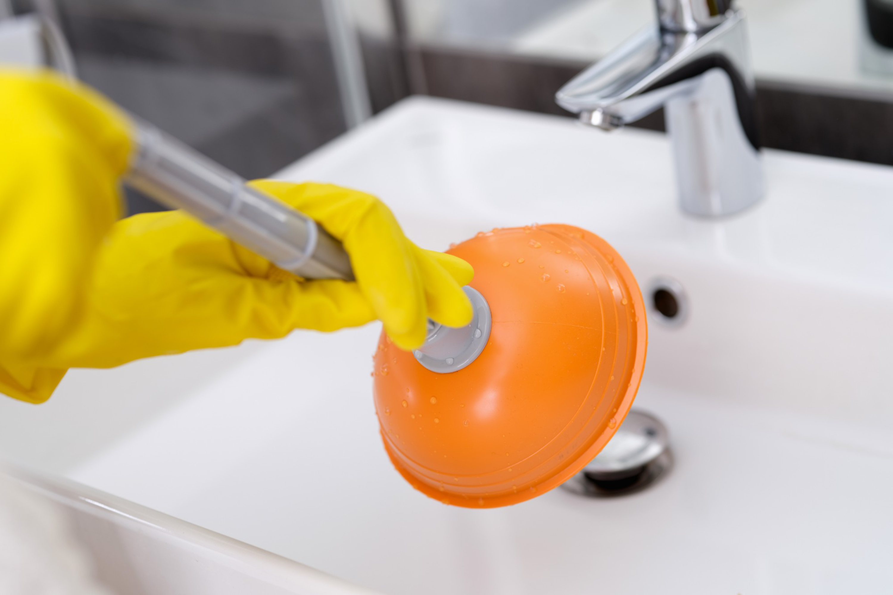 plumber-with-rubber-gloves-cleaning-sink-with-plunger-bathroom-closeup.jpg