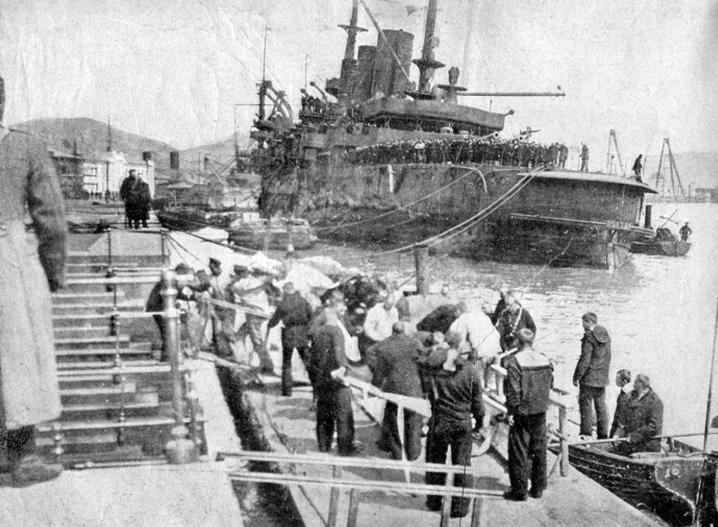 A Petropavlovszk túlélőinek egy csoportját partra teszik a kikötőben. A háttérben a szintén aknára futott, sérült és megdőlt Pobeda.
