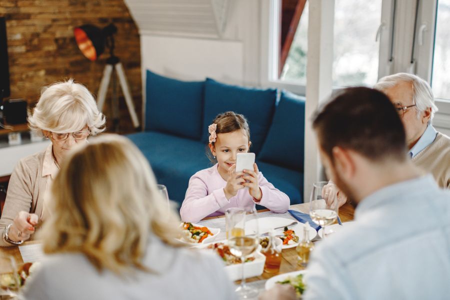 smiling-girl-sitting-dining-table-with-her-parents-grandparents-using-cell-phone.jpg