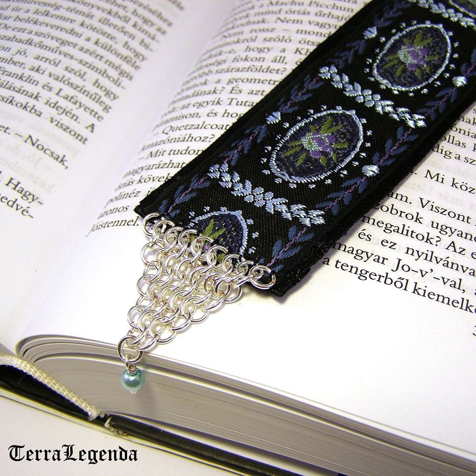 ‘Klasszicista hangulatú díszszalag és ezüstözött rézből készült chainmaille elem kombinációja, a végén egy aprócska kék üveggyönggyel.‘