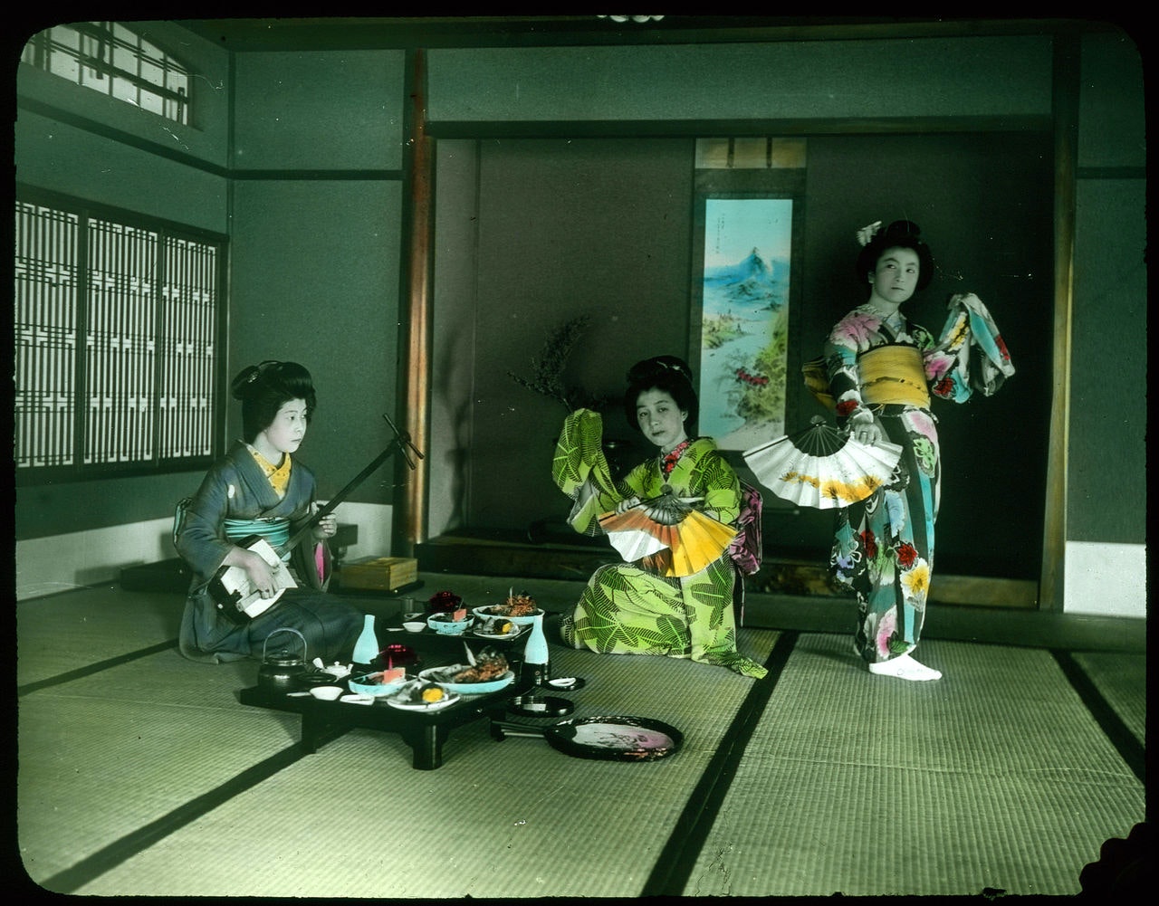 three_women_with_fans_musical_instrument_and_a_table_set_with_food_19763294649.jpg