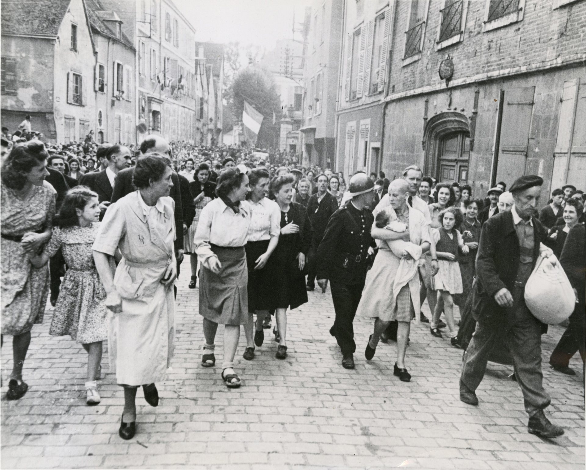Fotó: Robert Capa: Borotvált fejű francia nő, akinek gyereke született egy német katonától.<br />Chartres, Eure-et-Loir, 1944. augusztus 18. © Robert Capa / Magnum Photos <br /><br />Robert Capa 1944. augusztus 18-án a franciaországi Chartres városában készítette el világhírű fotóját, amelyet maga élete legjobb felvételének tartott.<br />„Döbbenetes volt a német katonától származó gyereket magához szorító nő és körülötte az eltorzult, gyűlölködő arcok. Hát ezt szeretem, mert sikerült emberi mélységeket megmutatni rajta.” (In: Markos György: Barátom, Capa)