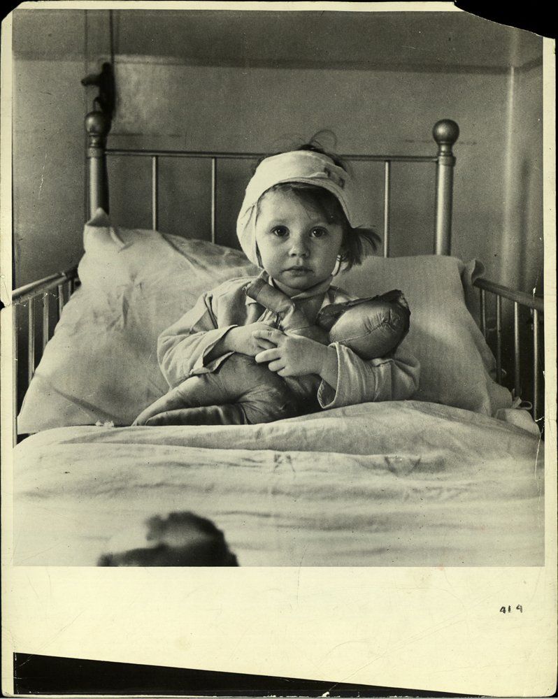 Fotó: Cecil Beaton: Eileen Dunne, Great Ormond Street Hospital, London, 1940 © Cecil Beaton/ Camera Press/ Redux<br /><br />A Brit Hírszerzési Minisztérium megbízásából készült ikonikus fotón egy sebesült kislányt láthatunk, aki bekötött fejjel szorongatja maciját egy nagy kórházi ágyon. A fotó egyik változata először a The Illustrated London News képeslap címlapján jelent meg 1940. szeptember 21-én az alábbi szöveggel: „A bombázás következményei: Göring London elleni támadásának gyerekáldozatai.” 