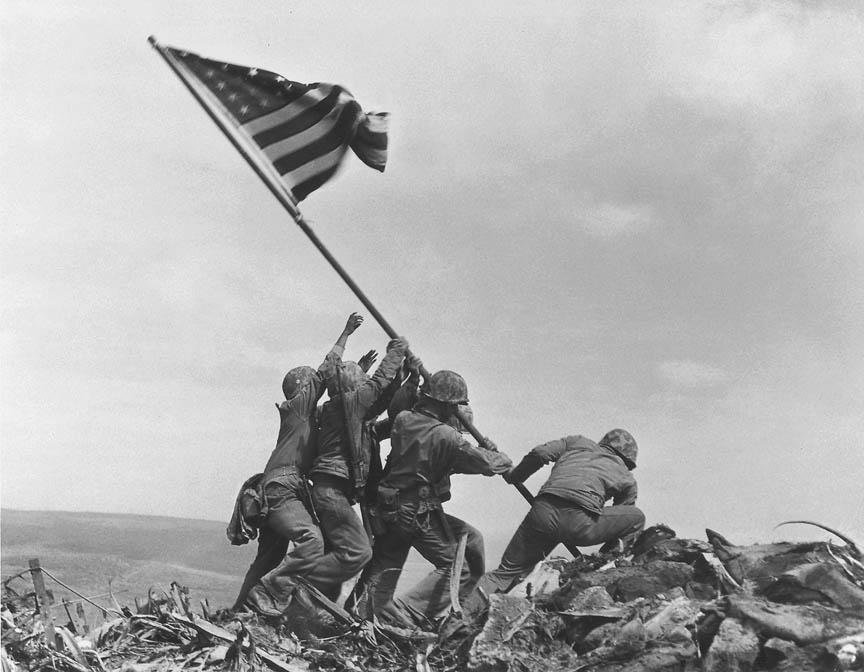 Fotó: Joe Rosenthal: Raising the Flag on Iwo Jima, 1945. február 23. AP Photo<br /><br />Itt is a történelem egy újrajátszott pillanatát látjuk. A délelötti zászlóállítás után Rosenthalnak sikerült az Easy Company hat tengerészgyalogosát rávennie az általa elképzelt feladatra. Ők állították fel a nagyobbra cserélt zászlót 12.30-kor, egy Rosenthal által megkomponált és beállított jelenet közben, s később ez a fotó járta be a világot, s vált a leghíresebb és legtöbbet reprodukált fotók egyikévé.
