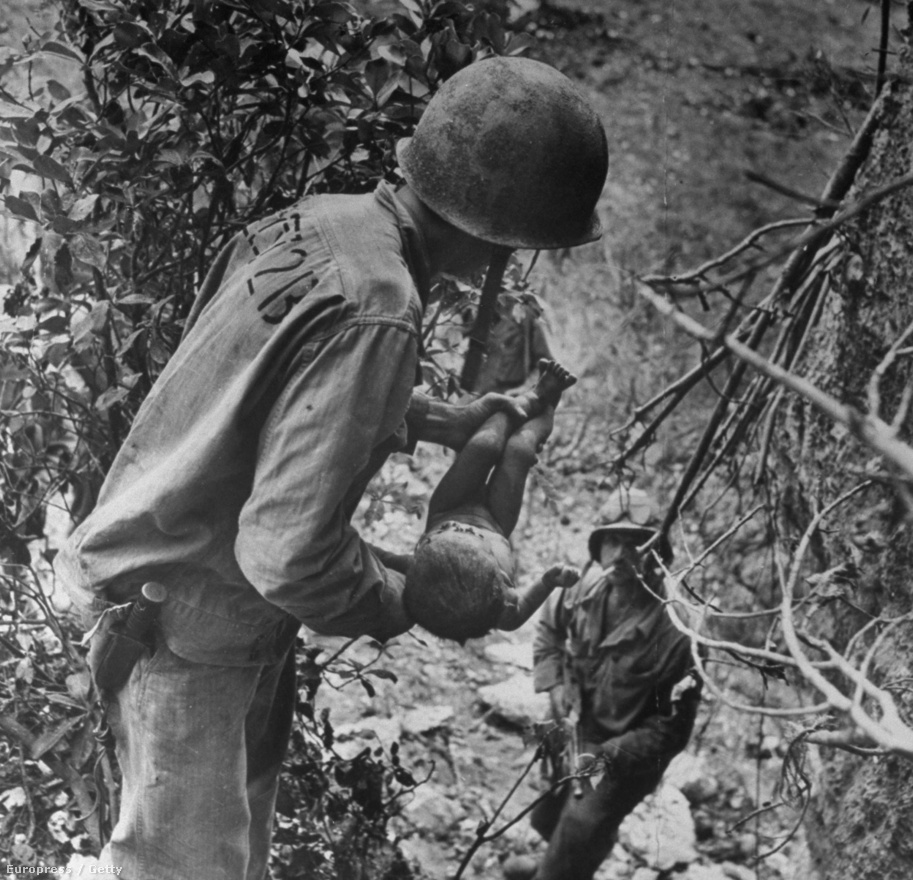 Fotó: W. Eugene Smith: Japán, 1944<br /><br />A fotográfust a világháborús felvételei tették igazán ismertté. Ezen a képen egy amerikai tengerészgyalogos egy súlyosan sérült csecsemőt ringat a második világháború japán frontján. A kis testet arccal lefelé találták egy barlangban, ahova a japánok az amerikai támadások elől húzódtak be. 