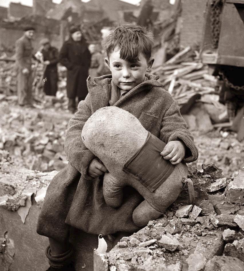 Fotó: Toni Frissell: Elárvult kisfiú ül otthona romjain, London, 1945 <br /><br />Toni Frissell 1945-ben, Londonban készítette világhírű fotóját, melyen a romokon üldögélő kisfiú kitömött állatfiguráját szorongatja. A kisfiú éppen játszani volt barátaival mikor a bombázást jelző szirénák megszólaltak, mire hazaért már csak a lerombolt otthonát találta meg, szülei és testvére a romok alatt lelték halálukat.