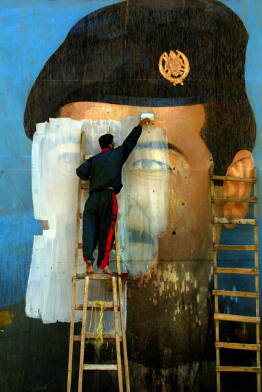 Fotó: Carolyn Cole: An image of Saddam Hussein, riddled with bullet holes, is painted over by Salem Yuel. Symbols of the leader disappeared quickly throughout Baghdad soon after US troops arrived in the city and took control, Baghdad, Iraq, April 2003<br />© Carolyn Cole / Los Angeles Times