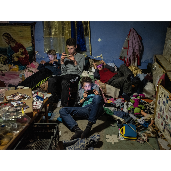 Társadalomábrázolás, dokumentarista fotográfia (egyedi)<br />3. helyezett<br />Móricz-Sabján Simon: Csanytelek<br />A Borsos fiúk mobiltelefonokkal játszanak a nappalijukban.<br />A nyolc fős Borsos család a Csongrád megyei Csanytelek településen él, életük, problémáik pedig tökéletes tükörképei Kelet-Magyarország problémáinak.