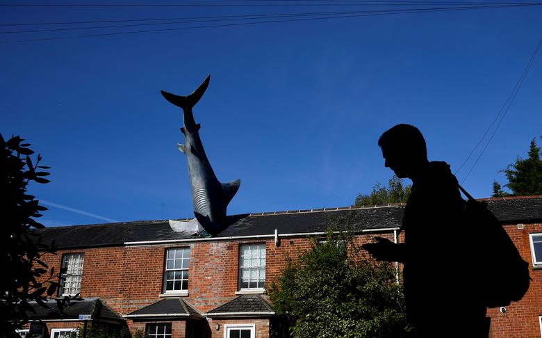 Fotó: Toby Melville: Egy férfi sétál az ‘Untitled 1986‘ nevű installáció mellett, amelyet általában ‘The Headington Shark‘-nak hívnak, és amelyet 1986-ban a nagaszaki támadás 41. évfordulójára készítettek. A cápa formájú szobor egy ház tetőjébe ágyazódik, Nagy-Britannia, Oxford, 2019. május 14. © Reuters/Toby Melville 