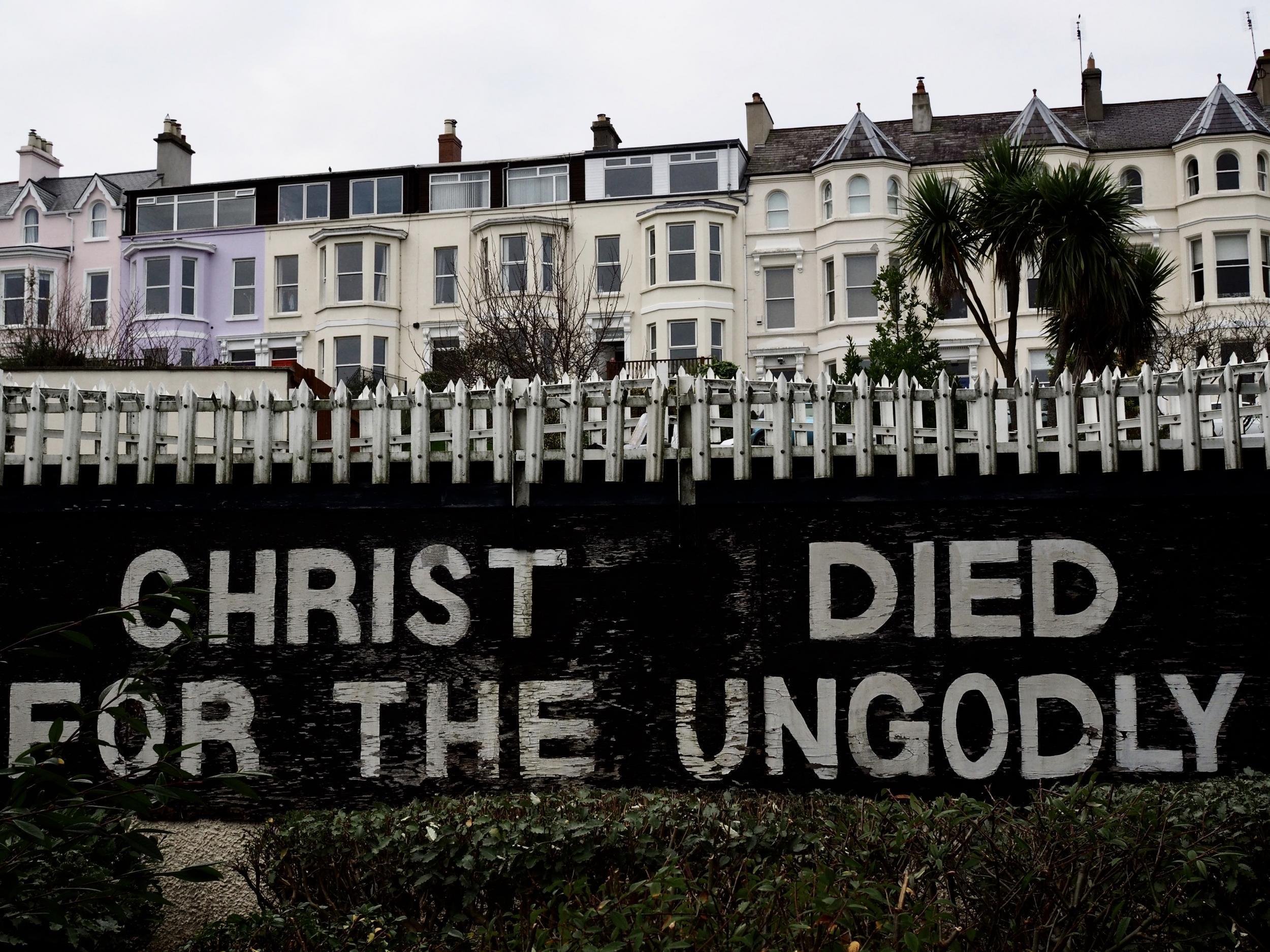 Bangor: „Krisztus az istentelenekért halt meg.” Erkölcsi ítélet, háttérben lakónegyeddel. Az üzenet mindenkit bevon a vallási narratívába: aki nem hisz, annak van a legtöbb adóssága. (Richard Morgan / The Independent)