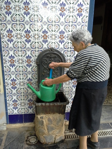 Senora Joaquina, éppen vizet vesz a falikútból a virágok locsolásához.