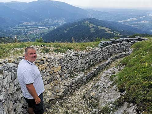 A szerző a Monte Palon lövészárkaiban 2021 nyarán. Kelet felé, a kép hátterében a Monte Tomba, mögötte a Piave völgye, balra az Alanói-medence Queróval