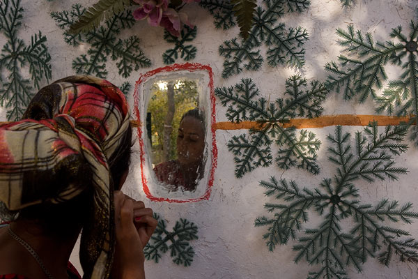 Egy fiatal nő a ház falába épitett tükörben nézi magát. A díszités műfenyő ágakból van. © Anzor Buharsky