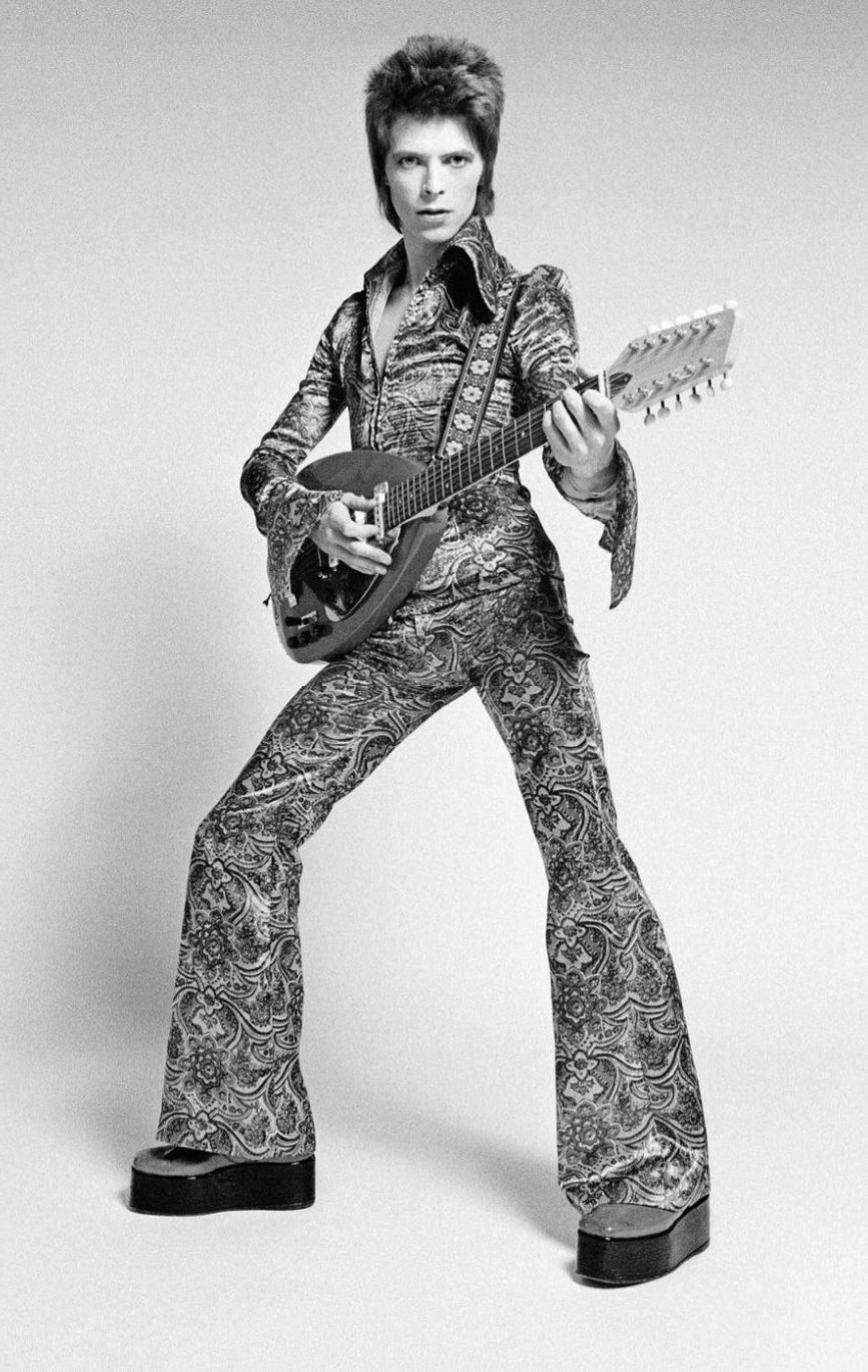 1972: Ziggy pózol a kamerának gitárral, magasított talpú cipõben, mintás kezeslábasban.
