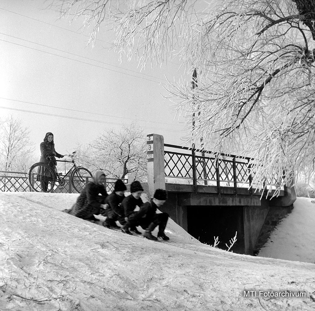 1958. január 27. Gyerekek összekapaszkodva csúsznak le a havas folyópart lejtőjén. A felvétel készítésének pontos helyszíne ismeretlen. MTI Fotó: Herczeg István