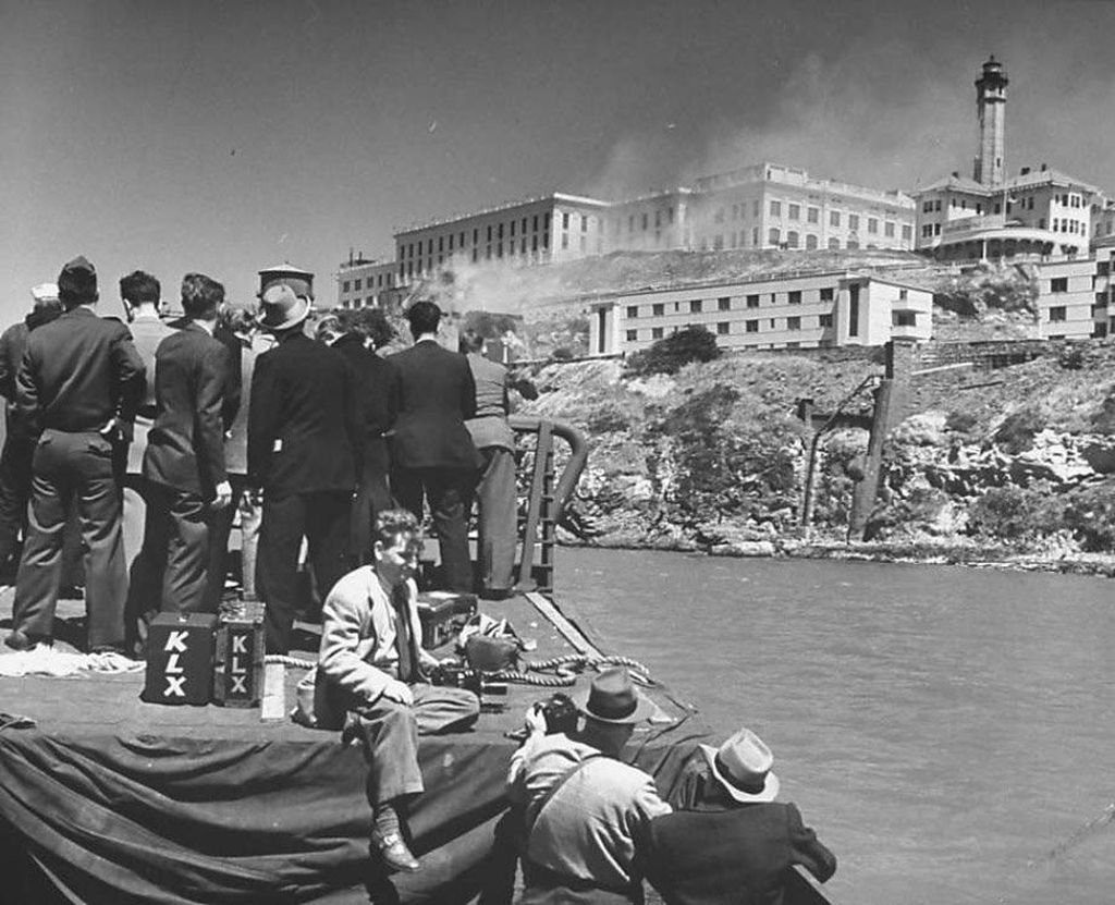press_and_spectators_stand_on_the_shore_and_view_the_carnage_of_the_prison_riots_1946.jpg