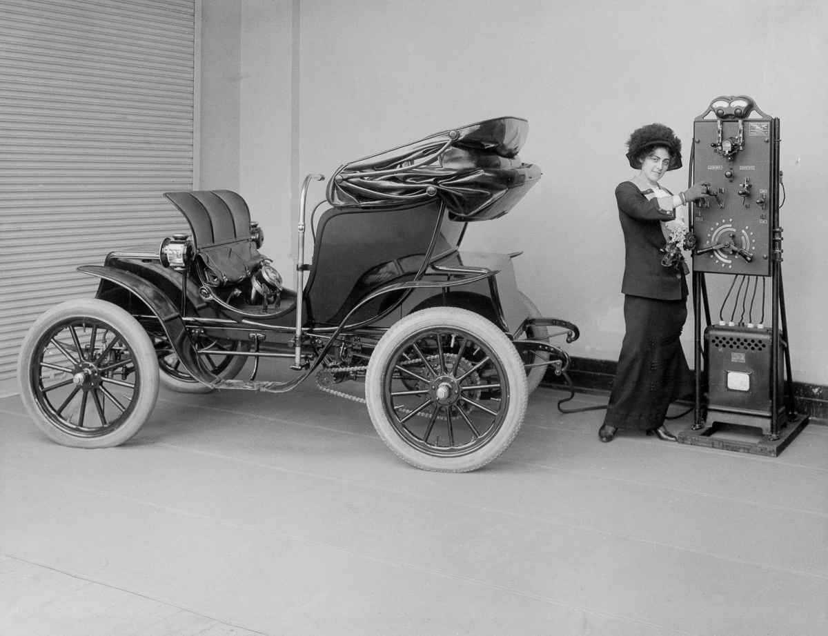 1912_a_woman_uses_a_hand_cranked_battery_charger_to_charge_her_electric_car.jpg
