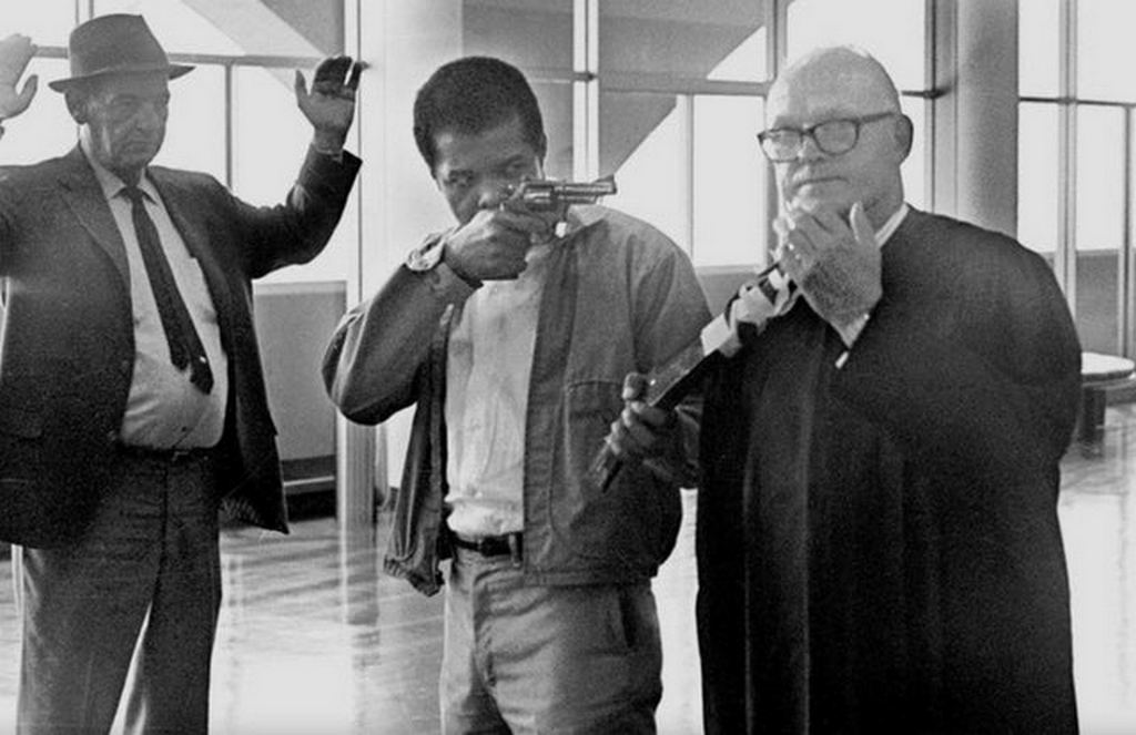1970_augusztus_7_james_mcclain_points_a_revolver_and_a_sawed-off_shotgun_that_is_taped_to_the_neck_of_judge_harold_j_haley_at_the_marin_county_courthouse.jpg